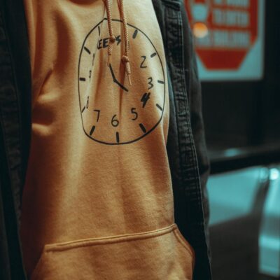 Close-up of a person wearing an orange hoodie with a clock design, showcasing urban style.