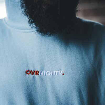 Detailed close-up of a blue hoodie with embroidered text and a partial view of a beard.