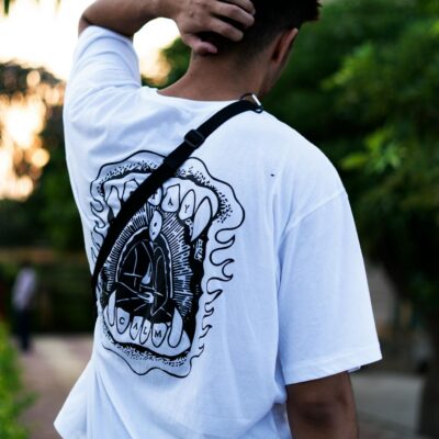Man in streetwear poses outdoors with hand on head, showing unique shirt design.